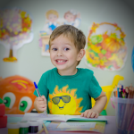 child smiling and drawing in drawing book with pen