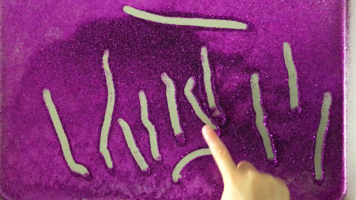 children writing in purple glitter sand