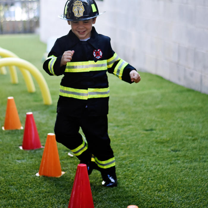 child dressed as a fireman running through cones