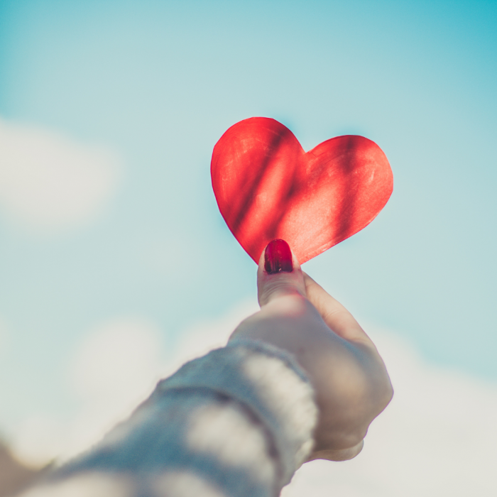 person holding red heart shaped paper cutout against blue sky